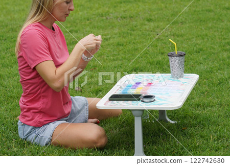 Young woman beading colorful bracelets outdoors in a park 122742680