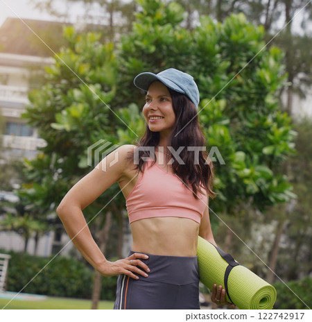 A young woman happily prepares to do yoga on a mat in a beautiful park. A young woman happily prepares to do yoga on a mat in a beautiful park. 122742917