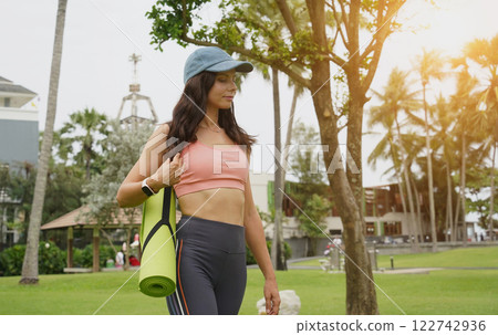 A young woman happily prepares to do yoga on a mat in a beautiful park. A young woman happily prepares to do yoga on a mat in a beautiful park. 122742936