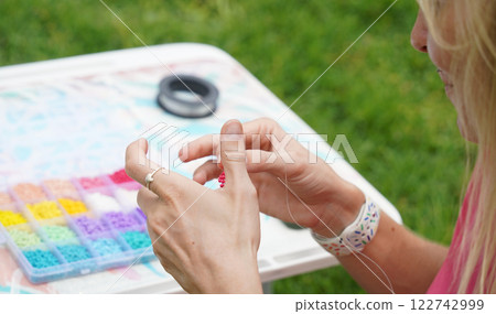 Young woman beading colorful bracelets outdoors in a park Young woman beading colorful bracelets outdoors in a park 122742999