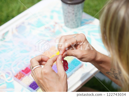 Young woman beading colorful bracelets outdoors in a park 122743034