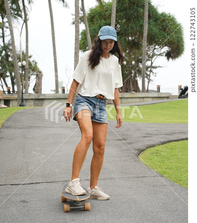 A young woman is skillfully riding a skateboard down a scenic park 122743105