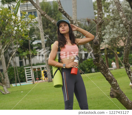 A young woman happily prepares to do yoga on a mat in a beautiful park. A young woman happily prepares to do yoga on a mat in a beautiful park. 122743127