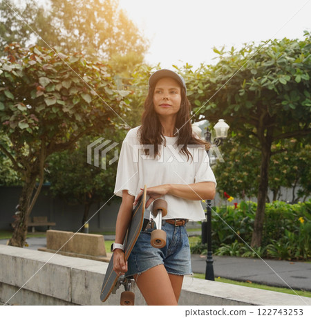 A woman is walking at the city park while carrying a skateboard in her hands 122743253