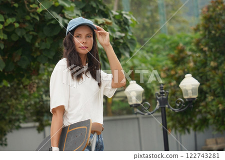 A woman is walking at the city park while carrying a skateboard in her hands 122743281