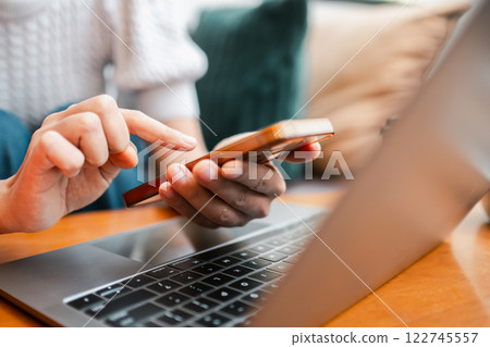 Person interacting with smartphone and laptop in a comfortable home environment, highlighting modern technology use. 122745557