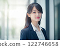 Smart working woman with a business suit is standing and posting in front of a blur office environment background created with generative AI technology 122746658