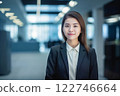 Smart working woman with a business suit is standing and posting in front of a blur office environment background created with generative AI technology 122746664