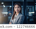 Smart working woman with a business suit is standing and posting in front of a blur office environment background created with generative AI technology 122746666