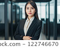 Smart working woman with a business suit is standing and posting in front of a blur office environment background created with generative AI technology 122746670