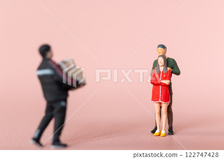 Miniature figurine scene depicting a man carrying presents towards a couple, with the woman appearing surprised 122747428