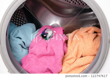 A woman's hand throws a laundry capsule into the washing machine 122747617
