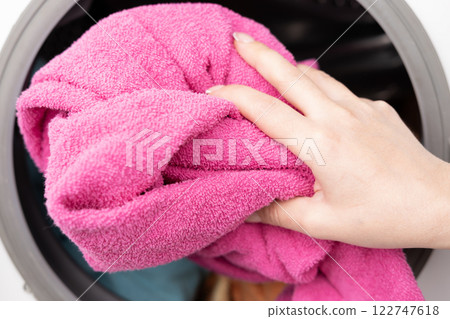A woman's hand throws a laundry capsule into the washing machine 122747618