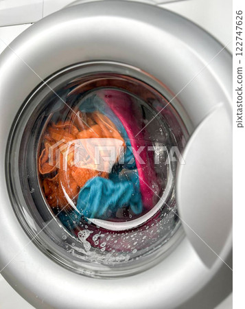 A woman's hand throws a laundry capsule into the washing machine 122747626