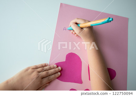 Child making heart shaped card with pink paper and letters Child making heart shaped card with pink paper and letters 122750094