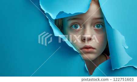 Blue eyed girl peeking through torn paper 122751603