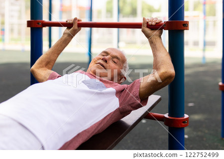 Old man doing leg raise exercise outdoors 122752499