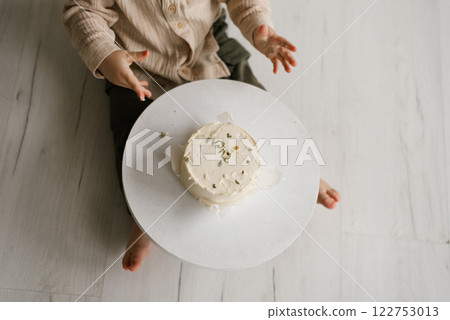 Baby is sitting on the floor in front of cake with the number one on it 122753013