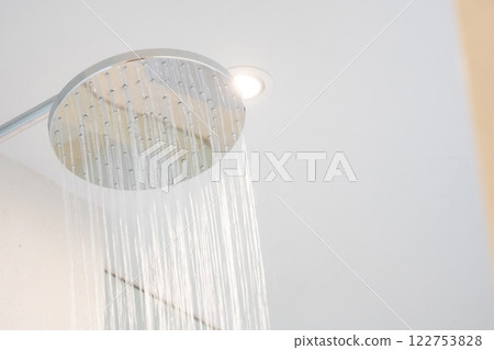 Cold Water was pouring out from a large shower in the bathroom with a glass window. Cold Water was pouring out from a large shower in the bathroom with a glass window. 122753828