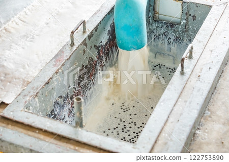 Milky white liquid gush out of the blue plastic industrial water pipe and flow through metal filter. 122753890