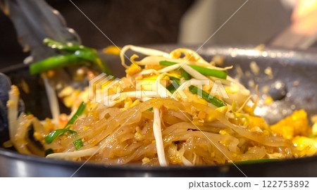 A cook stirs fry Pad Thai noodles in a pan with spatulas on electric stoves. Sauce dishes for cooking traditional Pad Thai. A cook stirs fry Pad Thai noodles in a pan with spatulas on electric stoves. Sauce dishes for cooking traditional Pad Thai. 122753892