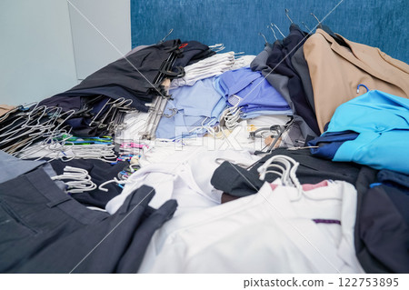 Untidy piles of clothes, arrange on a blue King bed. Women's suits come in a variety of colors, but men's pants were a dark tone color, all of this ready to rearrange in new closet. Untidy piles of clothes, arrange on a blue King bed. Women's suits come in a variety of colors, but men's pants were a dark tone color, all of this ready to rearrange in new closet. 122753895