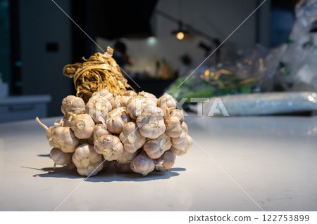 Garlic Bundle in studio light on the white marble surface table, prepare for a food demonstration behind. Garlic Bundle in studio light on the white marble surface table, prepare for a food demonstration behind. 122753899