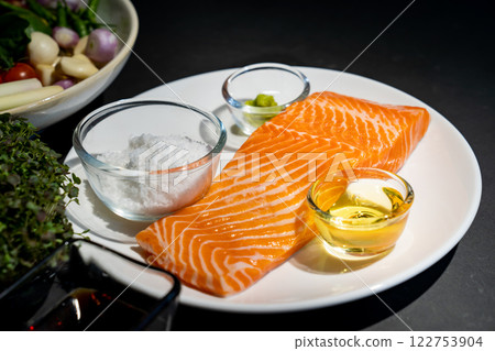 Salmon steak, Raw fillet of sea fish salmon or trout on white dish with salt, oil, and wasabi cream in studio light on dark background. Salmon steak, Raw fillet of sea fish salmon or trout on white dish with salt, oil, and wasabi cream in studio light on dark background. 122753904