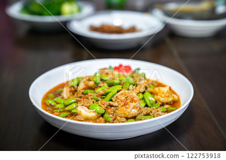Thai Stir-Fried Stink Beans with Shrimps and spicy shrimp paste sauce in white dish bowl on dark wood table. Thai Stir-Fried Stink Beans with Shrimps and spicy shrimp paste sauce in white dish bowl on dark wood table. 122753918