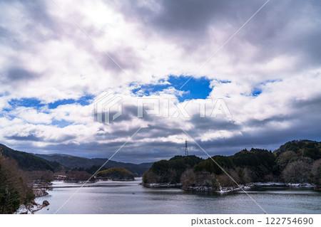 Snowy landscape of Nara Nunome Dam - A blue sky and its reflection on the lake surface, visible through the leaden clouds Snowy landscape of Nara Nunome Dam - A blue sky and its reflection on the lake surface, visible through the leaden clouds 122754690