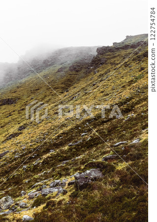 Misty mountains create an atmospheric landscape with rugged terrain and lush green slopes in early morning light. 122754784