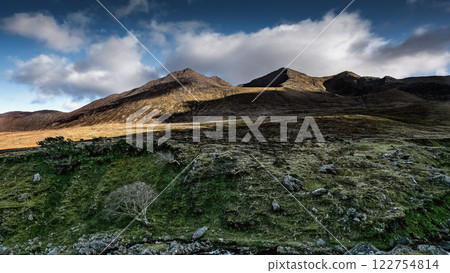 Mountain silhouette against dramatic clouds with lone tree in foreground at golden hour. Mountain silhouette against dramatic clouds with lone tree in foreground at golden hour. 122754814