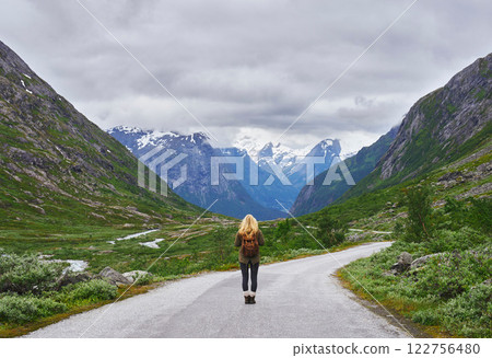 Adventure backpacking woman travels on road in epic majestic mountain snow landscape 122756480