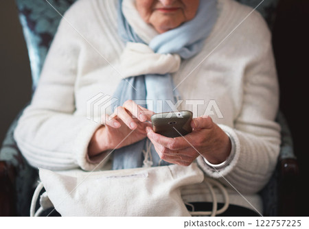 Senior woman, hands and smartphone for mobile app, armchair and online conversation at home. Elderly person, social media and typing on technology for communication, connection and website to relax 122757225