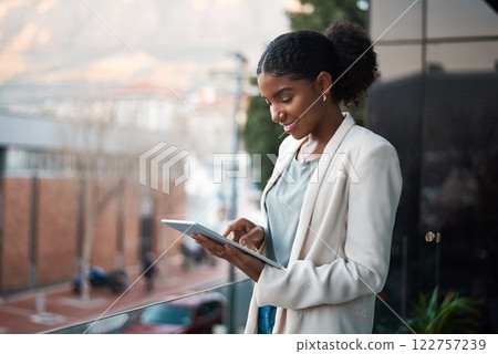 Business woman on a digital tablet outside a modern office alone. Smiling corporate worker looking at web and social media posts on a balcony. Female employee on a touchscreen device with copy space. 122757239