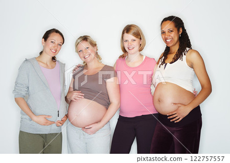 Pregnant, mother and friends with women in studio against a white background feeling happy with a smile. Pregnancy, health and wellness with positive female parents holding their abdomen together Pregnant, mother and friends with women in studio against a white background feeling happy with a smile. Pregnancy, health and wellness with positive female parents holding their abdomen together 122757557