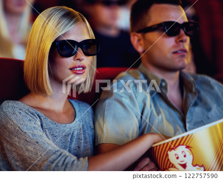 Couple, 3D movie and cinema of a man and woman sitting and eating popcorn together wearing glasses. People in a relationship watching a film in a theatre for indoor entertainment while having snacks. Couple, 3D movie and cinema of a man and woman sitting and eating popcorn together wearing glasses. People in a relationship watching a film in a theatre for indoor entertainment while having snacks. 122757590