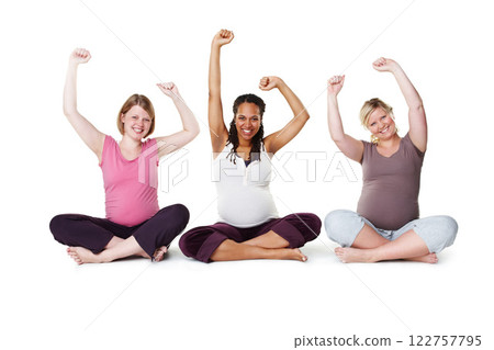 Pregnant, happy, and healthy, women sitting on the floor, arms raised in celebration of new life. Mothers, friends, and happiness during pregnancy, a group of future moms workout on white background 122757795
