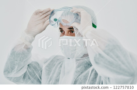 Covid, healthcare worker with safety protection clothing during first virus outbreak. A medical research professional in a hazmat suit and goggles preparing for work and staying safe during pandemic Covid, healthcare worker with safety protection clothing during first virus outbreak. A medical research professional in a hazmat suit and goggles preparing for work and staying safe during pandemic 122757810