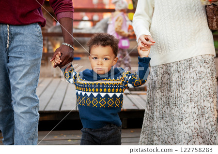 Young Child Boy Walks Hand In Hand With Parents Outdoors in Park, Looking At Camera. Family outing Young Child Boy Walks Hand In Hand With Parents Outdoors in Park, Looking At Camera. Family outing 122758283