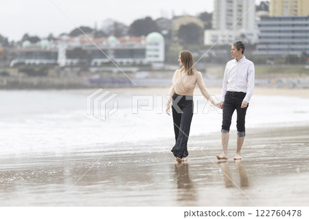 Couple walking barefoot on beach holding hands by city coastline 122760478