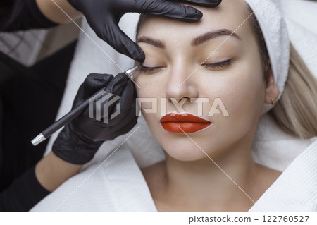 Permanent makeup. Cosmetologist tattoo artist applies a contour to the client's eyelid for subsequent application of eye tattooing 122760527