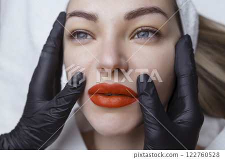 Permanent makeup. Lip tattooing. Bright red sexy lips in the hands of a cosmetologist in black gloves 122760528