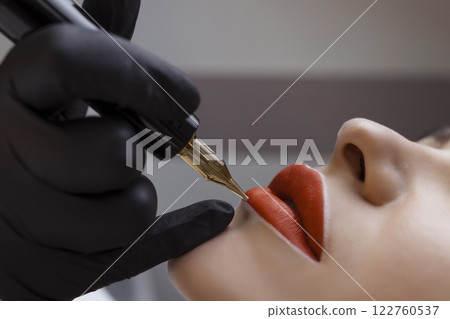 Cosmetologist makes permanent makeup on a woman's face. Specialist applies a tattoo on the patient's lips close-up Cosmetologist makes permanent makeup on a woman's face. Specialist applies a tattoo on the patient's lips close-up 122760537