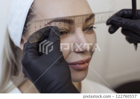 Eyebrow tattooing .Permanent eyebrow makeup master applies the contour with ruler on the client's eyebrow Eyebrow tattooing .Permanent eyebrow makeup master applies the contour with ruler on the client's eyebrow 122760557