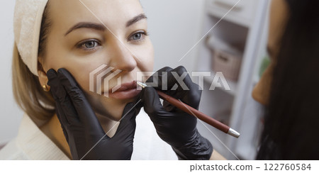 Young woman with permanent makeup on her lips in a cosmetologists salon. Permanent makeup tattoo. draw a line with a red lip pencil 122760584