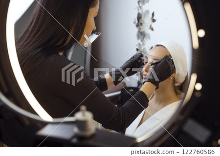 Eyebrow tattooing .Permanent eyebrow makeup master applies the contour with ruler on the client's eyebrow Eyebrow tattooing .Permanent eyebrow makeup master applies the contour with ruler on the client's eyebrow 122760586