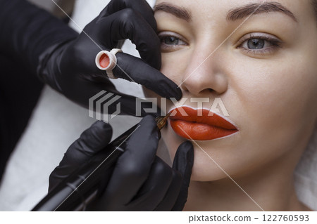 Cosmetologist makes permanent makeup on a woman's face. Specialist applies a tattoo on the patient's lips close-up Cosmetologist makes permanent makeup on a woman's face. Specialist applies a tattoo on the patient's lips close-up 122760593
