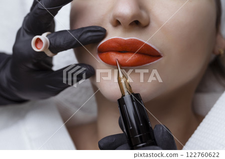 Cosmetologist makes permanent makeup on a woman's face. Specialist applies a tattoo on the patient's lips close-up Cosmetologist makes permanent makeup on a woman's face. Specialist applies a tattoo on the patient's lips close-up 122760622