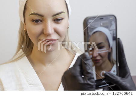 Permanent makeup. Tattoo artist photographs a client's lips on his phone 122760641